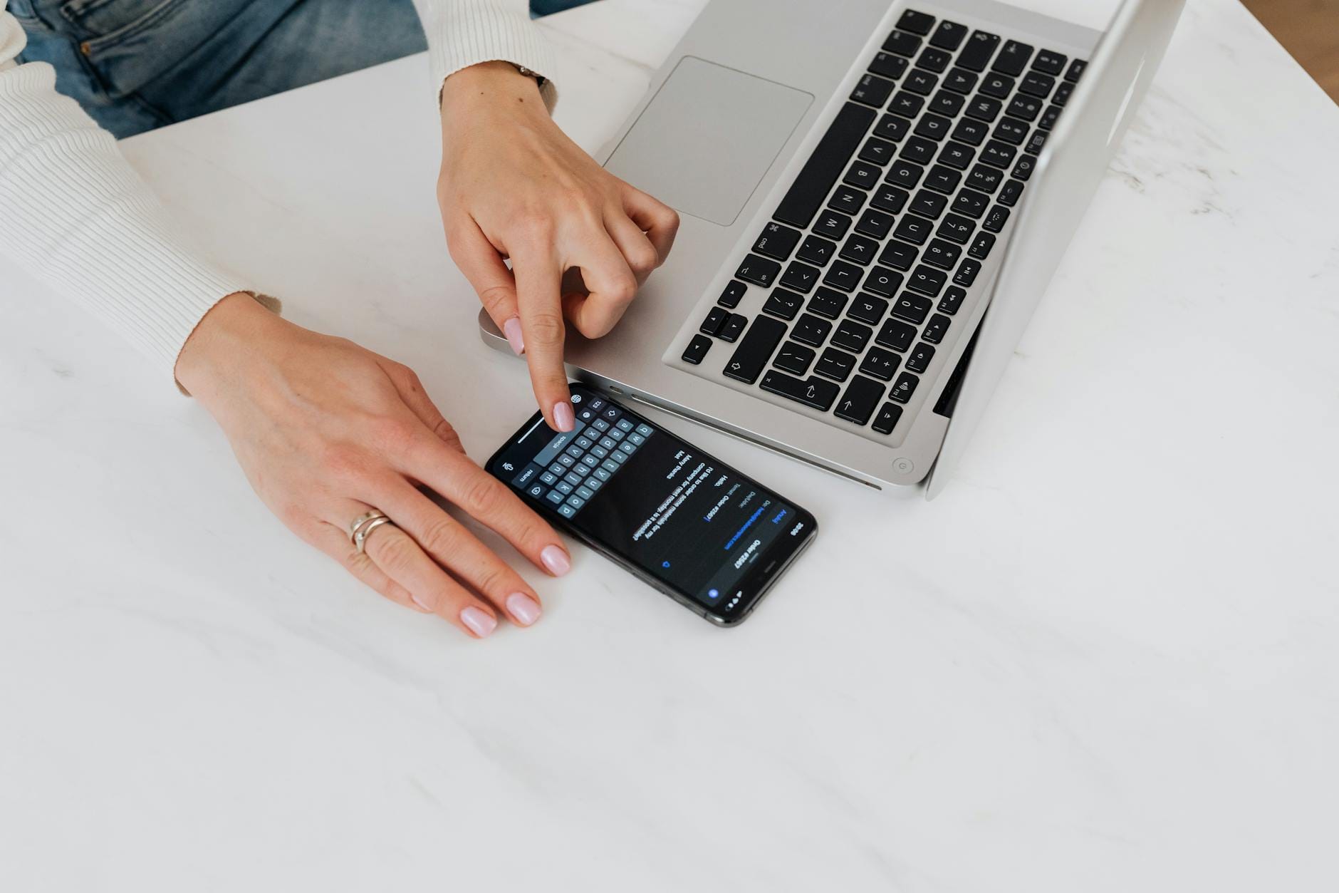 Dłonie korzystające ze smartfona i laptopa na białym biurku