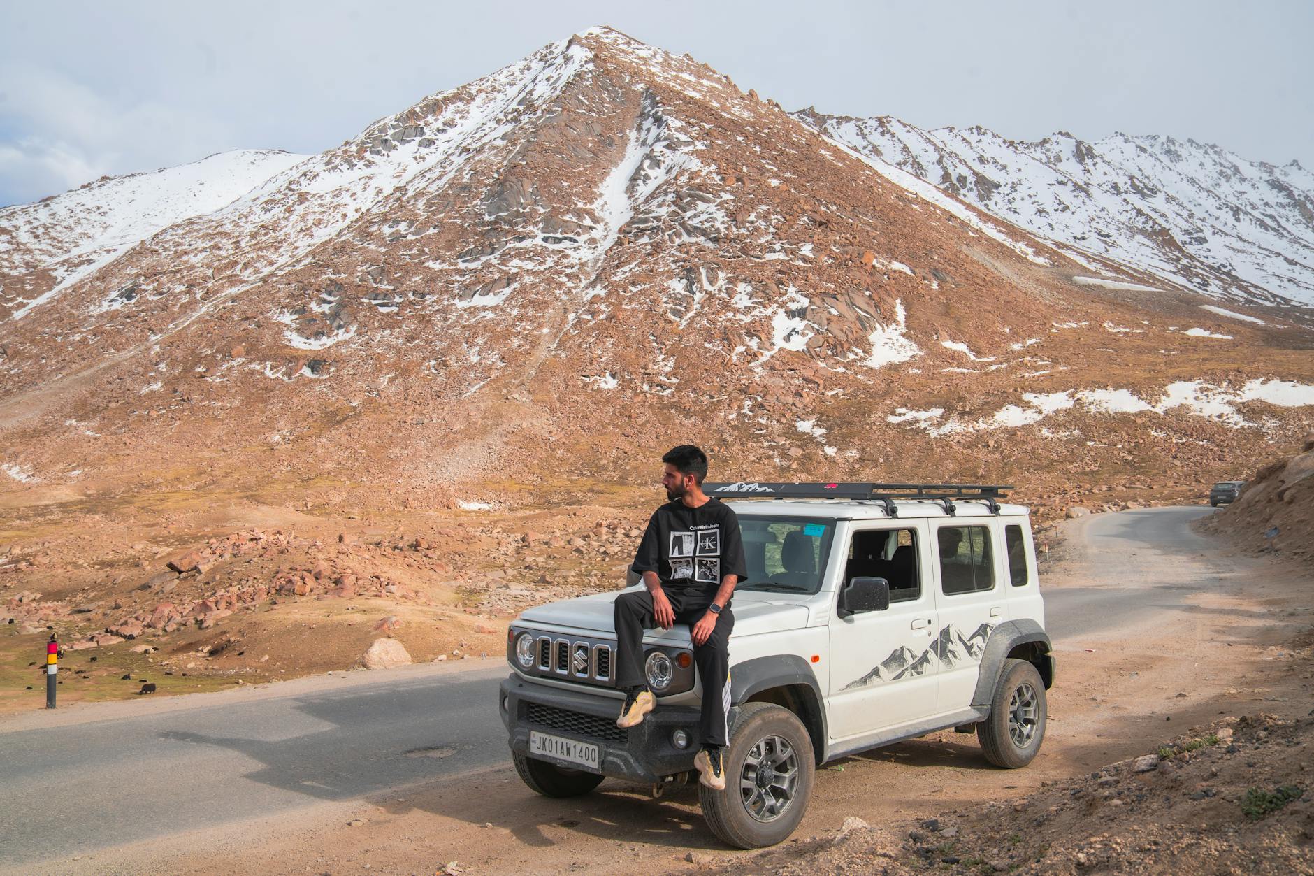 Mężczyzna siedzący na dachu SUV-a w ośnieżonych, skalistych górach